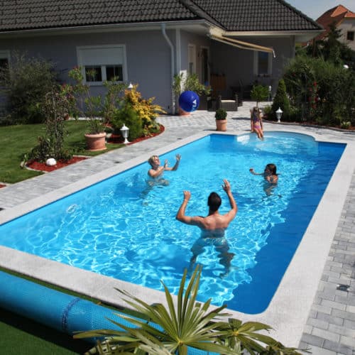 Cranpool Ihr Spezialist für Schwimmbecken im rechteckigen Schwimmbad befinden sich drei Personen, die Wasserball spielen. Auf der halbrunden vierstufigen Treppe sitzt eine Frau und sieht dem Geschehen zu. Das Schwimmbecken ist von Pflastersteinen umgeben. Auch kann manim garten eine Abdeckplane erkennen.