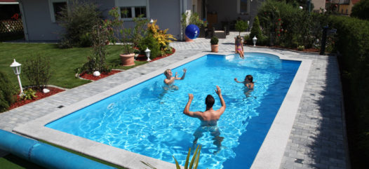 Cranpool Ihr Spezialist für Schwimmbecken im rechteckigen Schwimmbad befinden sich drei Personen, die Wasserball spielen. Auf der halbrunden vierstufigen Treppe sitzt eine Frau und sieht dem Geschehen zu. Das Schwimmbecken ist von Pflastersteinen umgeben. Auch kann manim garten eine Abdeckplane erkennen.