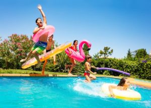 Kinder am Schwimmbecken und beim ins Wasser springen mit diversen Aufblasbaren Spielsachen