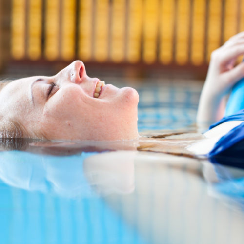 junge Frau im Pool, halb im Wasser, liegt auf einer Wassernudel im Schwimmbecken und genießt ihre Zeit im swimming pool